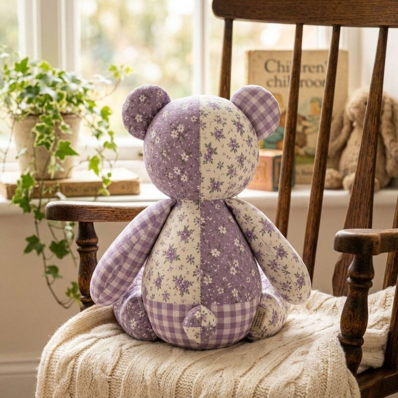 May include: A stuffed bear toy featuring a patchwork design of lavender and white fabrics. The bear is constructed from alternating panels of floral patterns and a classic gingham check print, with rounded ears and a small tail on the back.