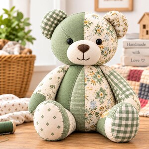 May include: A stuffed teddy bear constructed from patchwork fabric in shades of sage green, white, and cream. The bear features a mix of gingham, floral, and solid patterns, with black button eyes, a brown stitched nose, and a simple stitched mouth.