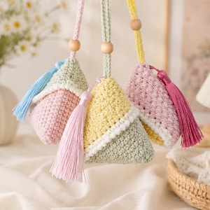 May include: Three triangular crochet pouches in pastel colors, each featuring a hanging loop with a wooden bead and a decorative silk tassel. The pouches are crafted with textured yarn in combinations of light pink, sage green, yellow, and white.
