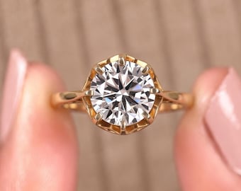Può includere: Un anello in oro con una pietra preziosa trasparente a taglio brillante rotondo in una montatura a sei griffe. La fascia è sottile e lucida, con una finitura in oro giallo metallizzato che contrasta con la pietra bianca sfaccettata centrale.