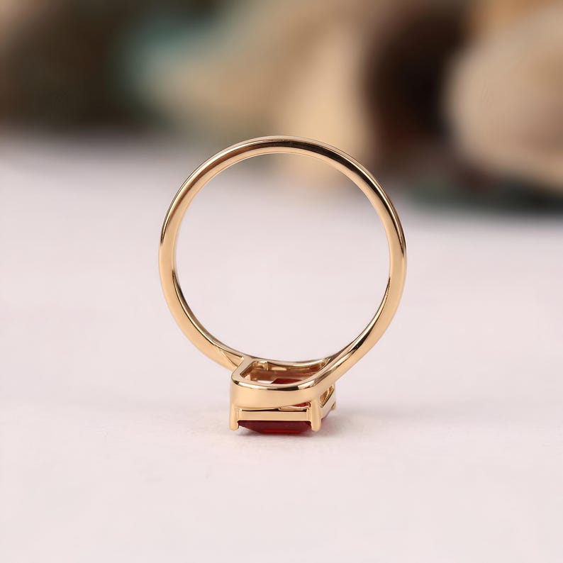 Upright rear view of a yellow gold bypass ring showing the polished circular shank and the underside of its deep red rectangular gemstone setting.