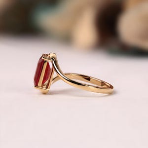Side profile of a rectangular ruby red gemstone ring showing its faceted stone, elevated open gallery and smoothly curved yellow gold bypass shank.