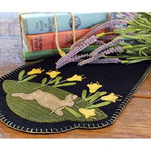 May include: A black felt table runner with a green felt bunny and yellow felt flowers. The runner has a scalloped edge and is decorated with a stitched design.