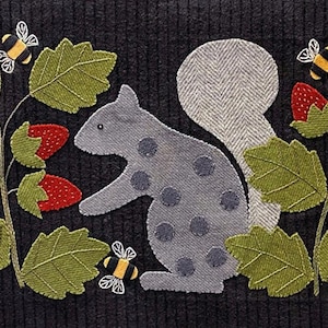 May include: A rectangular black textile wall hanging featuring a central gray squirrel with dark gray polka dots and a light gray tail. The squirrel is flanked by green leaves, red strawberries, and three small yellow and black bumblebees.