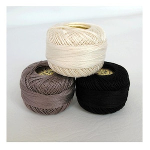 May include: Three balls of yarn in different colors: white, brown, and black. The yarn is wound into balls and ready for knitting or crocheting.