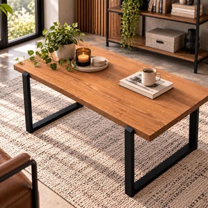 May include: A rectangular coffee table with a natural wood grain top and black metal U-shaped legs. On the table sits a potted green plant, a candle in a glass jar, a small stack of coasters, and a white mug resting on a book.
