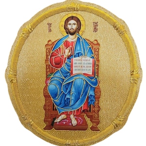 May include: A circular religious icon featuring a central figure seated on a throne, wearing a red tunic and blue mantle. The figure holds an open book with Cyrillic text. The background is gold with a textured border and decorative gold trim.