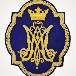 Könnte beinhalten: Ein dunkelblauer bestickter Aufnäher mit einem Monogramm aus goldenem Metallic-Garn, das die ineinander verschlungenen Buchstaben M und A zeigt. Über dem Monogramm befindet sich eine goldene Krone. Das Design hat einen goldenen Rand.