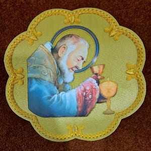 May include: A gold-toned, scalloped-edge patch featuring a printed image of a bearded figure in blue and red vestments holding a chalice. The border is decorated with intricate gold embroidery, and a gold chalice is depicted next to the figure.
