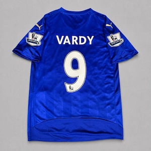 以下が含まれることがあります： 背面に白い文字でVARDY、数字で9がプリントされたロイヤルブルーの半袖スポーツジャージ。肩には金色のPumaロゴがあり、両袖にはライオンのエンブレムが描かれたBarclays Premier Leagueのワッペンが付いています。