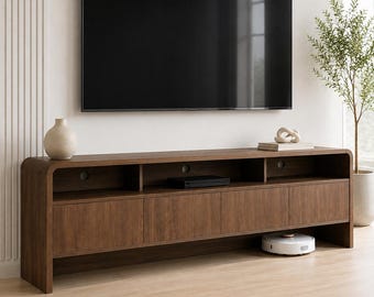 May include: A long, dark wood media console featuring rounded edges, four cabinet doors, and three open storage compartments with circular cable management holes. A large flat-screen television is mounted on the wall above the console.