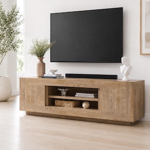 May include: A rectangular light brown wooden media console featuring two side cabinets and an open central shelving unit with two levels. The console is positioned beneath a large flat-screen television and a black soundbar on the top surface.