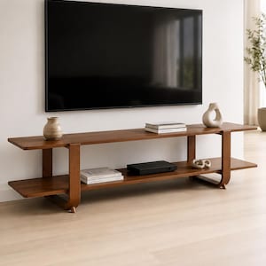 May include: A long, low-profile wooden media console featuring two horizontal shelves supported by curved, rounded legs. The dark brown wood grain finish complements the flat-screen television mounted on the wall above the unit.