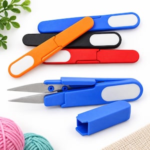 Peut inclure: Un ensemble de ciseaux pliants en bleu, orange, noir et rouge. Chaque paire possède un manche en plastique avec un accent ovale blanc. Une paire bleue est présentée en position ouverte avec des lames en métal argenté et un capuchon assorti.