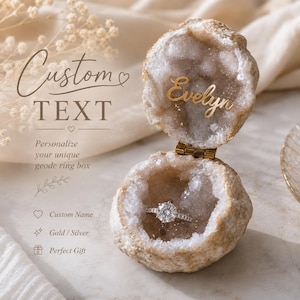 Op de afbeelding: Een open geode ringdoosje met een ruwe, natuurlijke buitenkant en een sprankelende kristallijne binnenkant. De naam Evelyn staat in gouden letters in het deksel geschreven. Een zilveren diamanten ring ligt in de basis van het doosje.