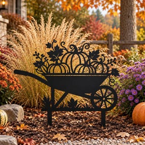Könnte beinhalten: Ein schwarzer Metall-Gartenstecker in Form einer Schubkarre, gefüllt mit Kürbissen und Herbstblättern. Das Silhouetten-Design verfügt über ein einzelnes Rad, einen Griff und einen flachen Fuß zum Einstecken in den Boden, passend zum Erntethema.