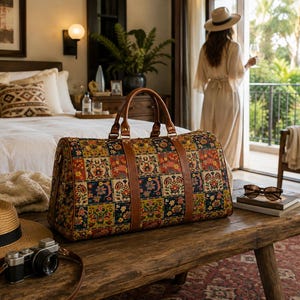 May include: A rectangular duffel bag featuring a multi-coloured patchwork pattern with floral and paisley motifs, accented by brown leather handles and trim. The bag has a structured base and two top handles, showcasing a vibrant, detailed textile design.