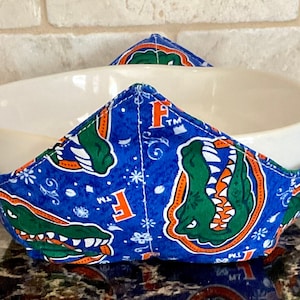 May include: A blue and green bowl cozy with an alligator design and the letters "F" and "TM".