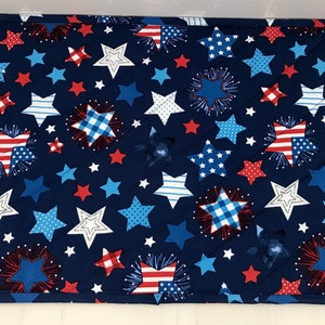 May include: A navy blue quilted placemat featuring a patriotic star pattern in red, white, and blue. The design includes various star shapes, fireworks, and American flag motifs, perfect for Independence Day celebrations.