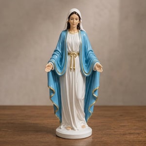 Könnte beinhalten: Eine stehende Figur der Jungfrau Maria in einem weißen Gewand und einem blauen Mantel mit goldenem Saum. Die Figur trägt ein weißes Kopftuch, eine goldfarbene Taillenkordel und hat die Arme mit geöffneten Handflächen ausgestreckt.