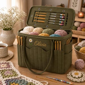 May include: An olive green fabric yarn storage bag with a daisy embroidery and the name Olivia stitched on the front. The open lid reveals organized slots for crochet hooks, while the main compartment holds multiple balls of colorful yarn.