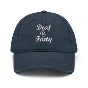 Peut inclure: Une casquette de baseball bleu marine avec une finition usée et vieillie. L'avant présente un texte brodé en blanc qui indique "Deaf @ Forty" dans une police cursive. La casquette possède une visière courbée et une calotte structurée.