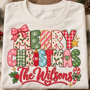Può includere: Una t-shirt color crema con il testo Merry Christmas The Wilsons in un carattere colorato e fantasia. Le lettere sono decorate con motivi a quadri, pois, agrifoglio e fiocchi di neve. Sono presenti un fiocco rosa, una stella gialla e un bastoncino di zucchero.