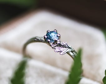 May include: A delicate silver ring with a blue gemstone and a leaf design, displayed in a velvet ring box.