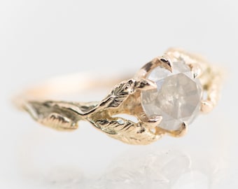 May include: A gold ring with a delicate leaf design and a round, grey diamond.