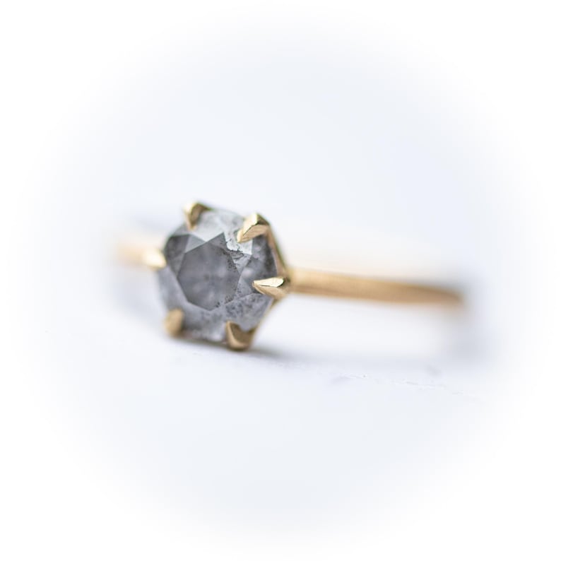 May include: A gold ring with a gray, hexagonal, rough-cut diamond.
