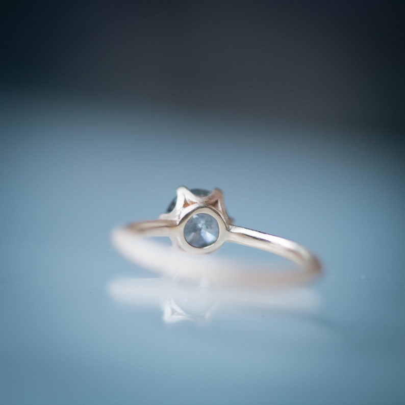May include: A delicate gold ring with a small, round, light blue gemstone set in a prong setting.