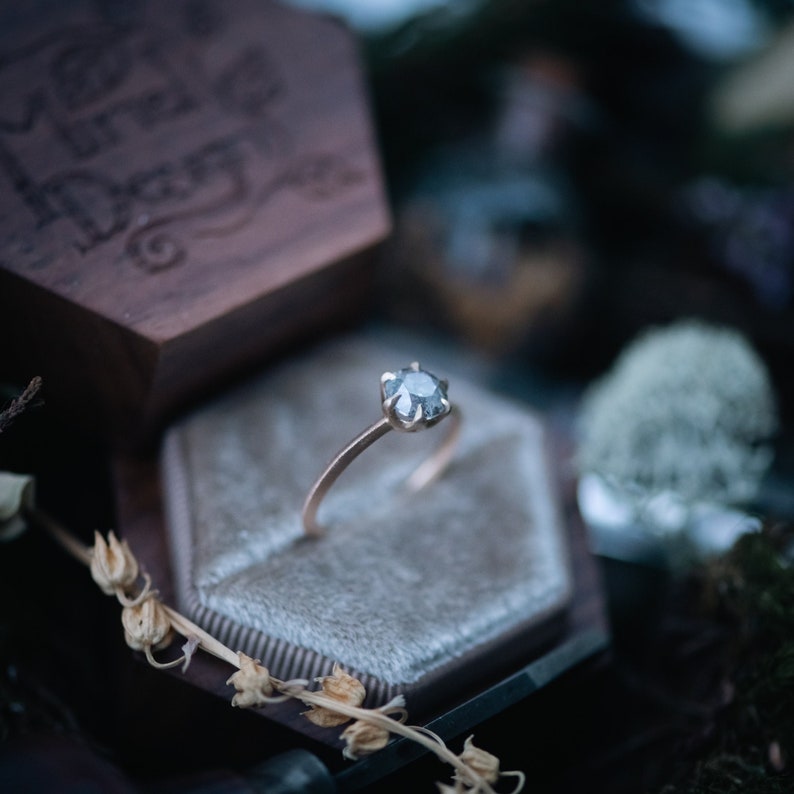 May include: A silver ring with a gray gemstone set in a gold band, displayed in a velvet ring box.