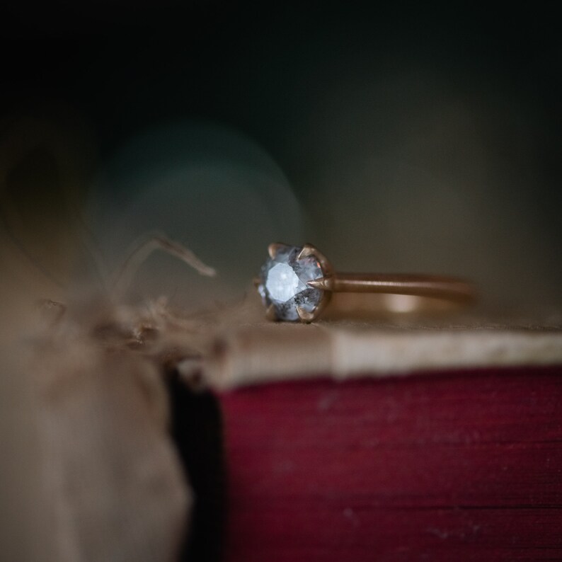 May include: A gold ring with a large, clear, faceted diamond set in a prong setting. The ring is resting on a brown, textured surface.