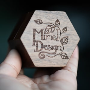 May include: A hexagonal wooden box with a laser-engraved design featuring the text "Muriel Design" and stylized leaves.