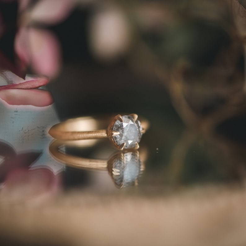 May include: A gold ring with a round, gray diamond set in a prong setting.