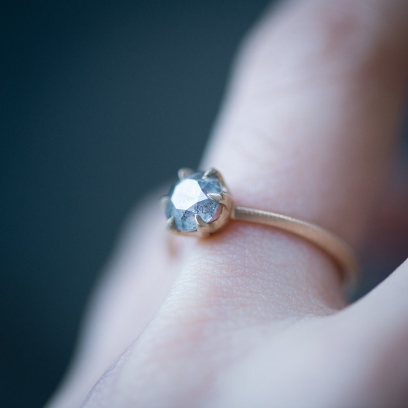 May include: A gold ring with a large, clear, faceted gemstone. The gemstone has a gray hue and is set in a prong setting.