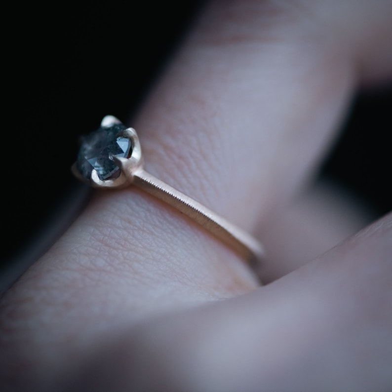 May include: A gold ring with a dark gray gemstone set in a prong setting.