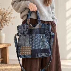 May include: A patchwork tote bag featuring various blue and brown fabric squares with diverse patterns including geometric shapes, floral motifs, and plaid designs. The bag includes two top handles and a long shoulder strap, all made from the same fabric.