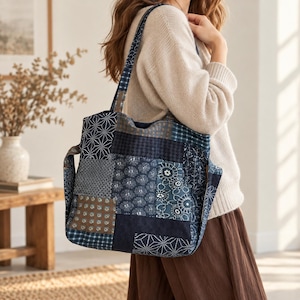 May include: A patchwork tote bag featuring various shades of blue and indigo fabric squares with diverse white geometric, floral, and grid patterns. The bag includes two shoulder straps and a rectangular body constructed from stitched textile panels.