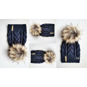 May include: Three navy blue knitted hats with faux fur pom-poms. The hats have a cable knit pattern and a small gold label.