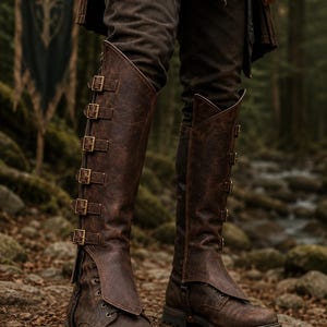 May include: A pair of knee-high brown leather boots featuring a distressed finish, a lace-up front, and a tall outer flap secured by five brass-toned metal buckles running vertically along the side of each boot, set on a thick lugged sole.