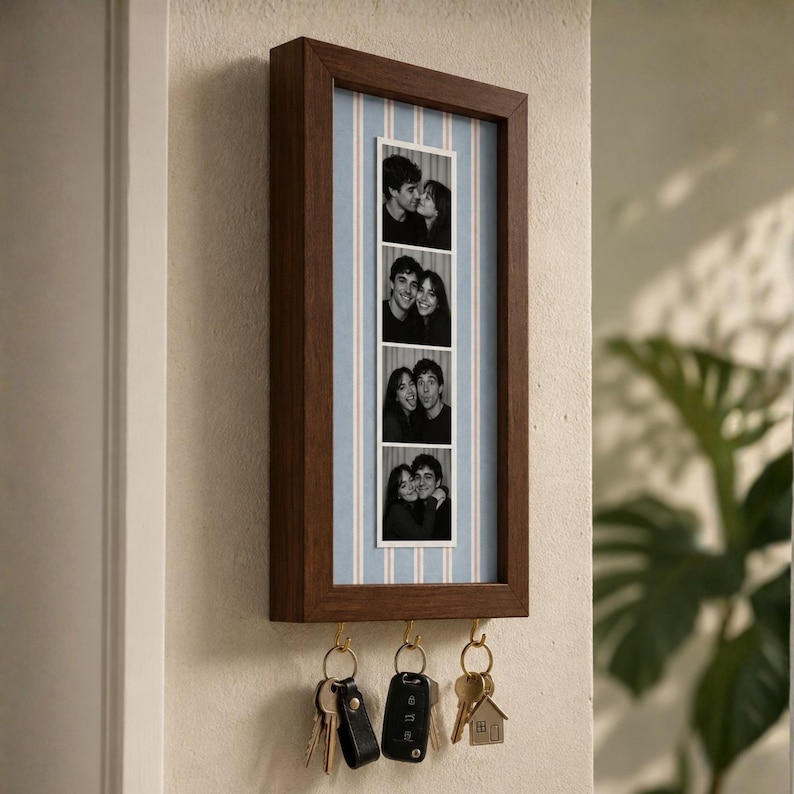May include: A rectangular dark wood wall-mounted key holder featuring a vertical photo strip of a couple in black and white. The background behind the photo strip is light blue with thin white vertical stripes. Three gold hooks hold keys.