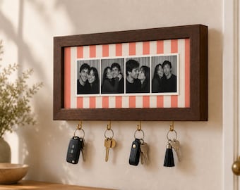 May include: A rectangular dark brown wooden wall-mounted key holder featuring a central horizontal display area with a coral and white striped background. Four gold-toned metal hooks hang below, each holding a set of keys with various keychains.
