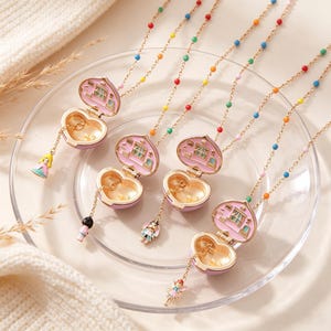 May include: Four gold-tone necklaces featuring heart-shaped lockets that open to reveal a miniature room interior. Each locket is attached to a chain with colorful beads and a small dangling charm depicting a character in a dress or outfit.