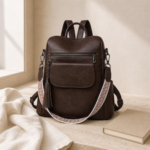 Pode incluir: Uma mochila castanho-escura com acabamento liso, um bolso frontal com aba e uma alça superior. Inclui uma alça de ombro destacável com um padrão geométrico tecido multicolorido e uma borla de couro castanho-escuro a condizer na lateral.