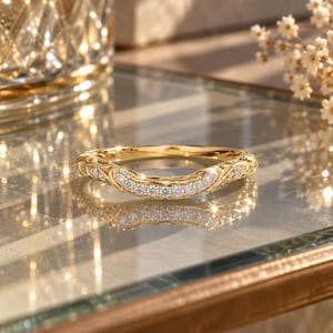 Op de afbeelding: Een gebogen gouden ring met een reeks kleine, ronde, heldere stenen gezet langs de voorste boog. Het metalen oppervlak vertoont ingewikkelde, gegraveerde krulpatronen die zich over de ring uitstrekken, wat zorgt voor een gedetailleerd en getextureerd uiterlijk.