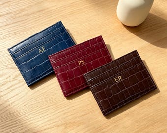 Può includere: Tre porta carte rettangolari con texture a stampa coccodrillo in blu navy, bordeaux e marrone scuro. Ogni porta carte presenta iniziali dorate in rilievo: AF sul blu, PS sul bordeaux e ER sul porta carte di colore marrone scuro.