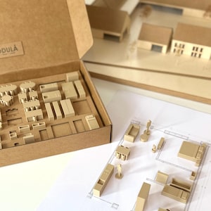 May include: A brown cardboard box containing an assortment of small, light tan wooden furniture miniatures. The box lid features the text MODULA. Several of these miniature furniture pieces are arranged on a white architectural floor plan.