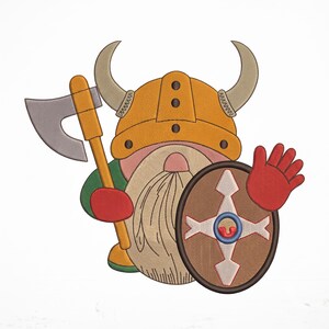 Könnte beinhalten: Ein gestickter Aufnäher mit einem Cartoon-Gnom als Wikinger verkleidet. Der Gnom trägt einen gelben gehörnten Helm, hält eine graue Axt mit gelbem Stiel und trägt einen runden braunen Schild mit weißem Kreuzmuster. Der Gnom hat einen langen Bart.