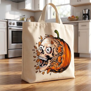 May include: A beige canvas tote bag featuring a graphic illustration of a human skull emerging from a bright orange pumpkin. The skull has wide, startled eyes and an open mouth, with orange pumpkin fragments scattered around the central design.